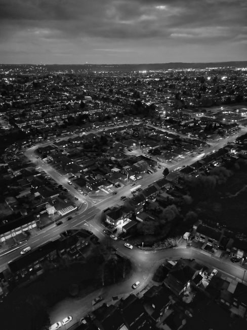 A black and white aerial photograph showing a large suburban residential area with rows of houses and streets extending into the distance. In the foreground, there is a sports field with goalposts and